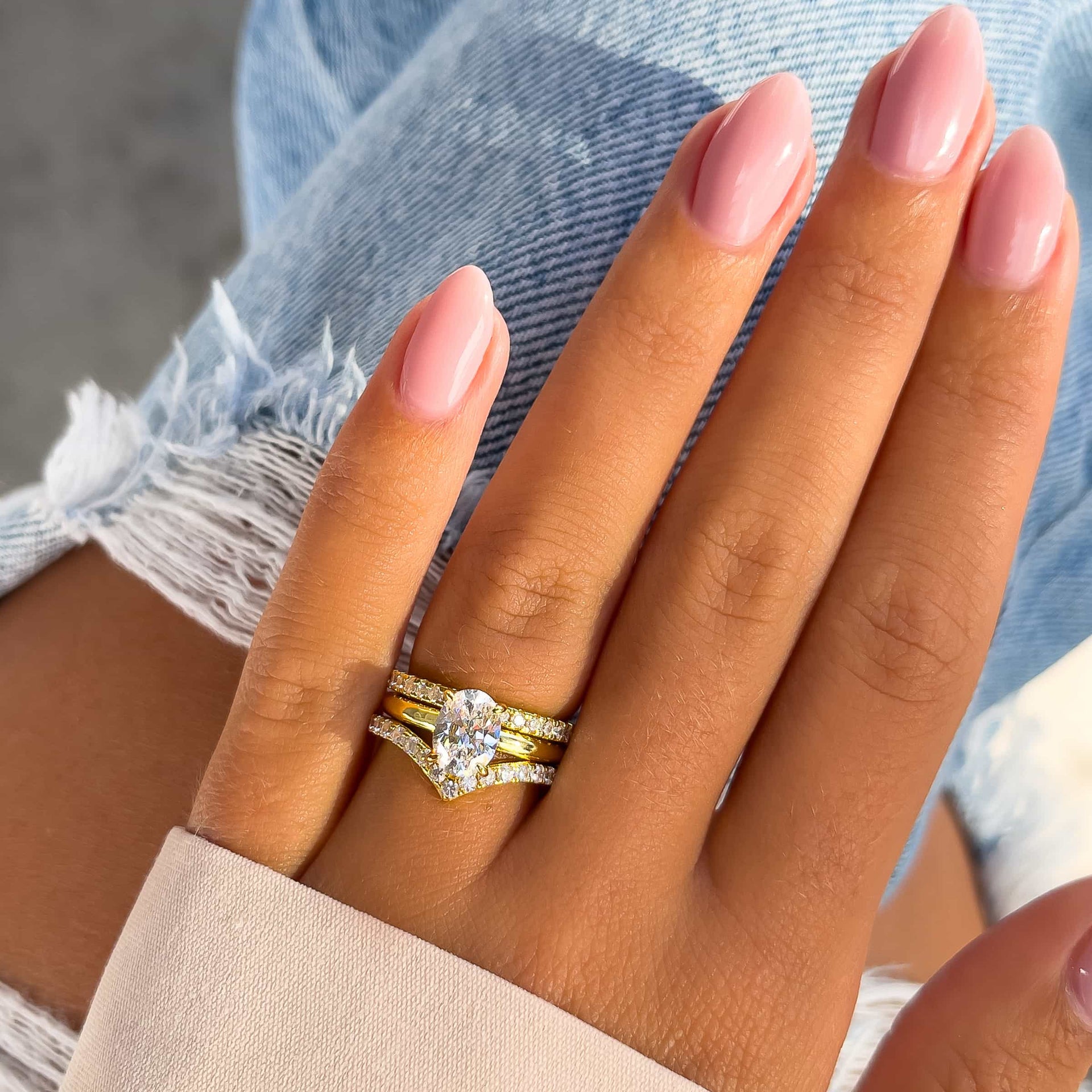 sparkling gold solitaire engagement ring and wedding bands on model hand with tan sleeve and blue jeans