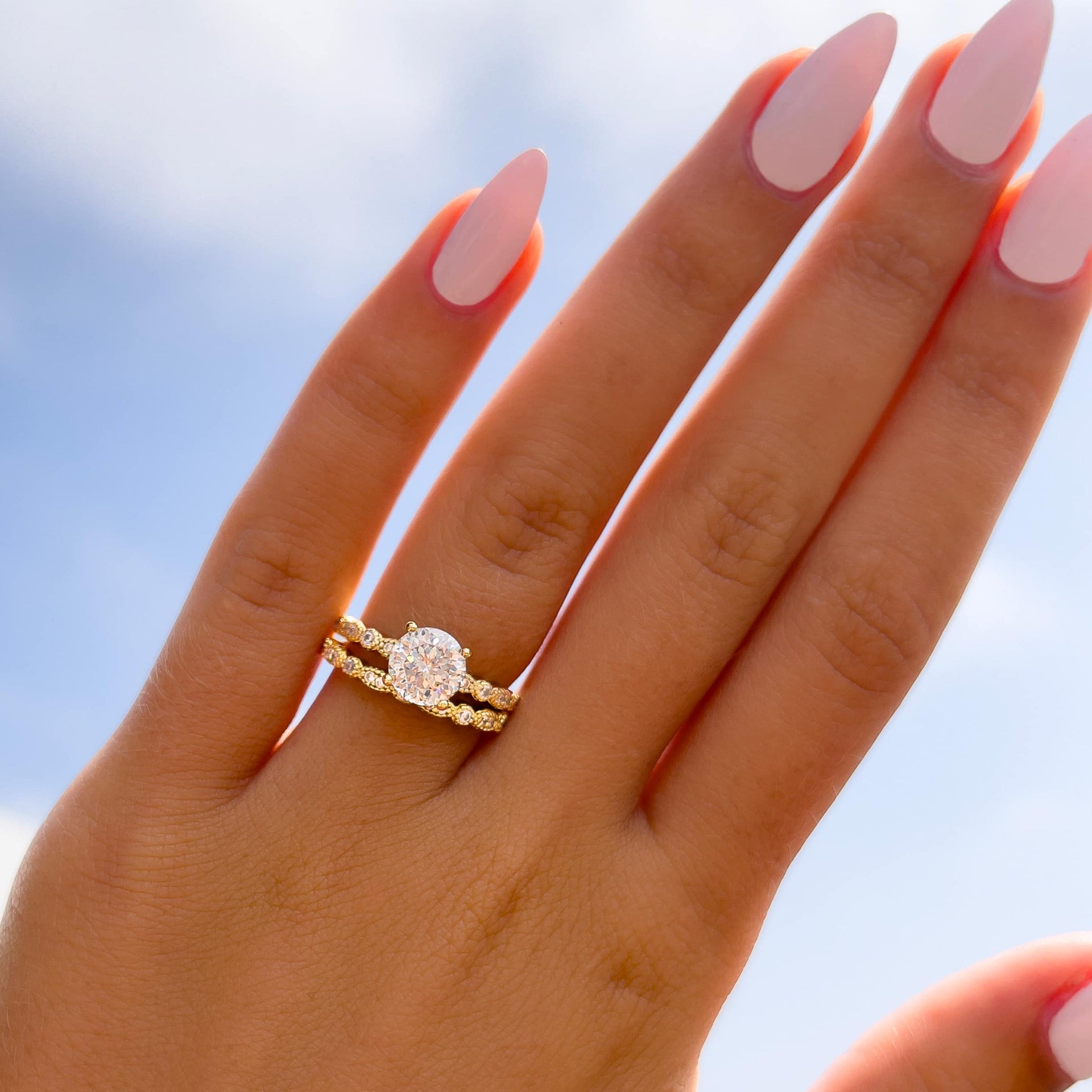 gold round cut vintage style engagement ring paired with matching gold wedding band on model with light pink nails