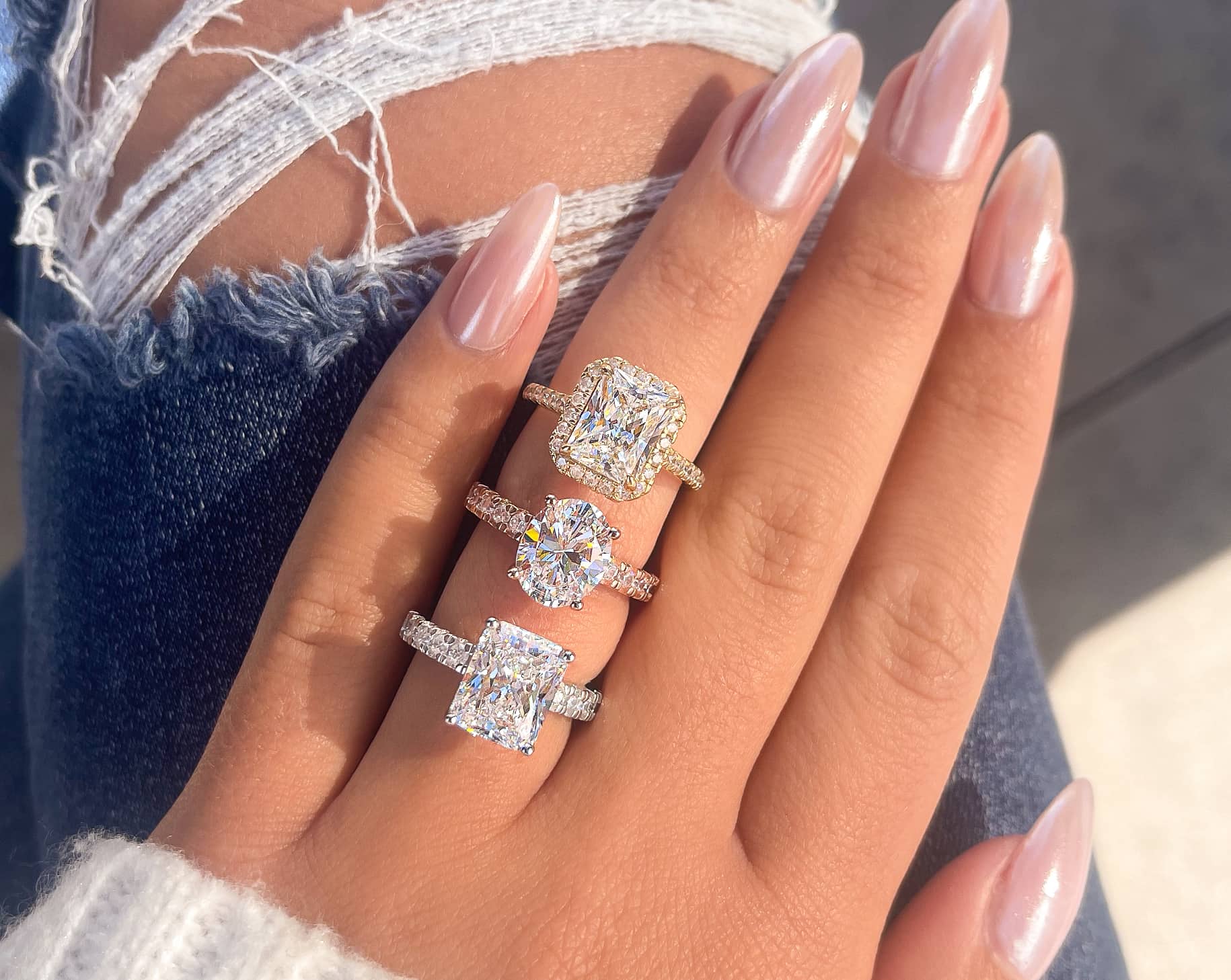 woman wearing silver, gold, and rose gold trendy engagement rings by jeans