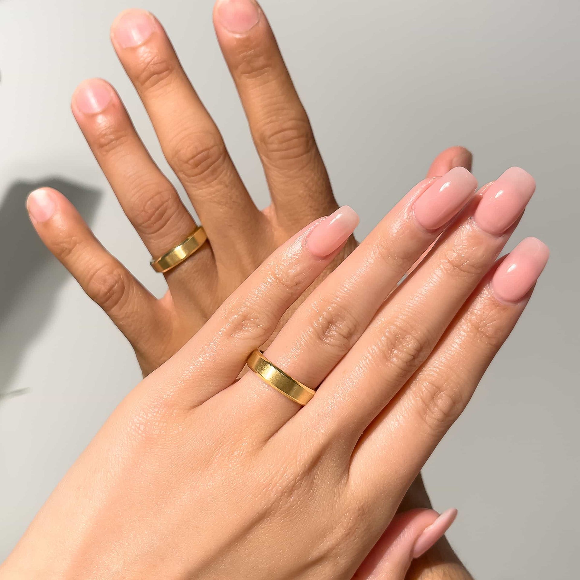 Couple point of view wearing unisex wedding band in gold against gray background