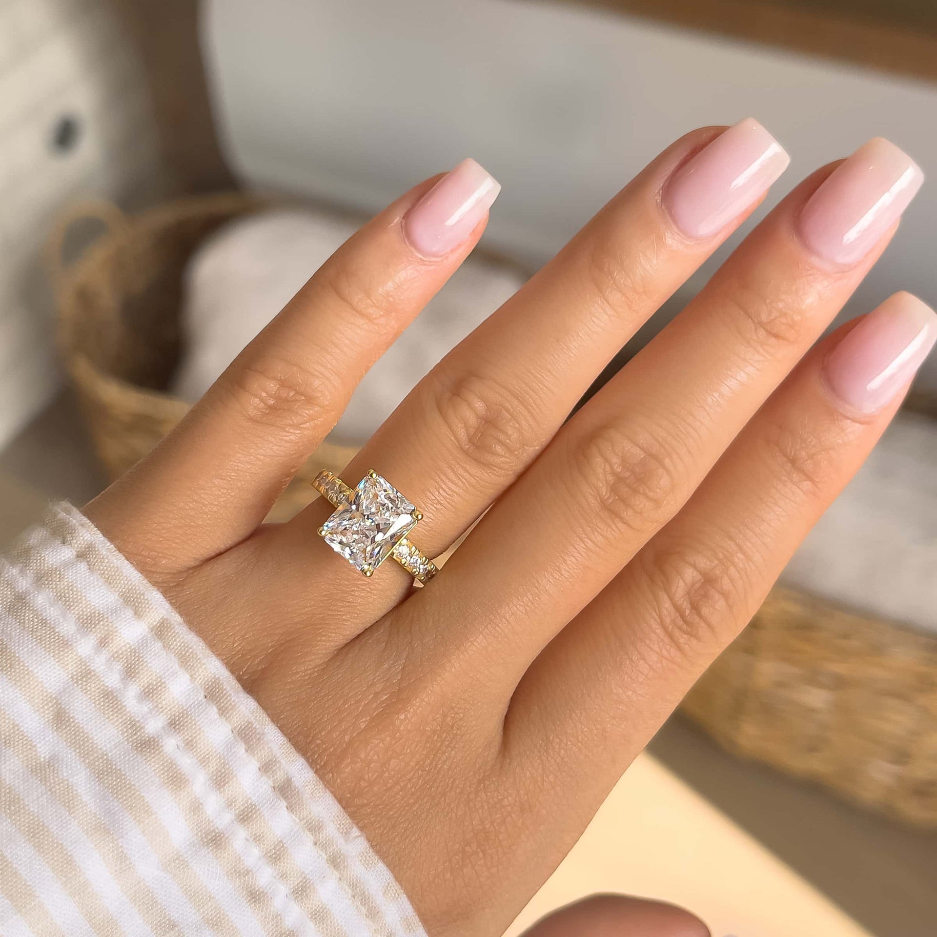 beautiful gold radiant cut engagement ring on model's hand with light pink nails and brown white striped top