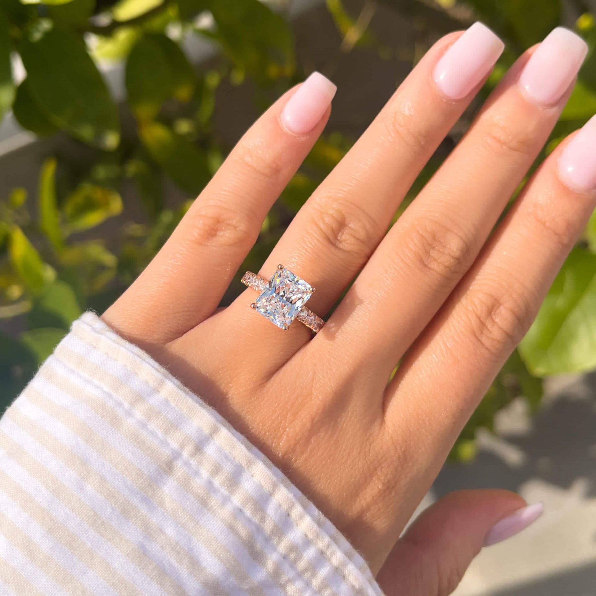 affordable radiant cut engagement ring in rose gold on female hand with white and brown sleeve