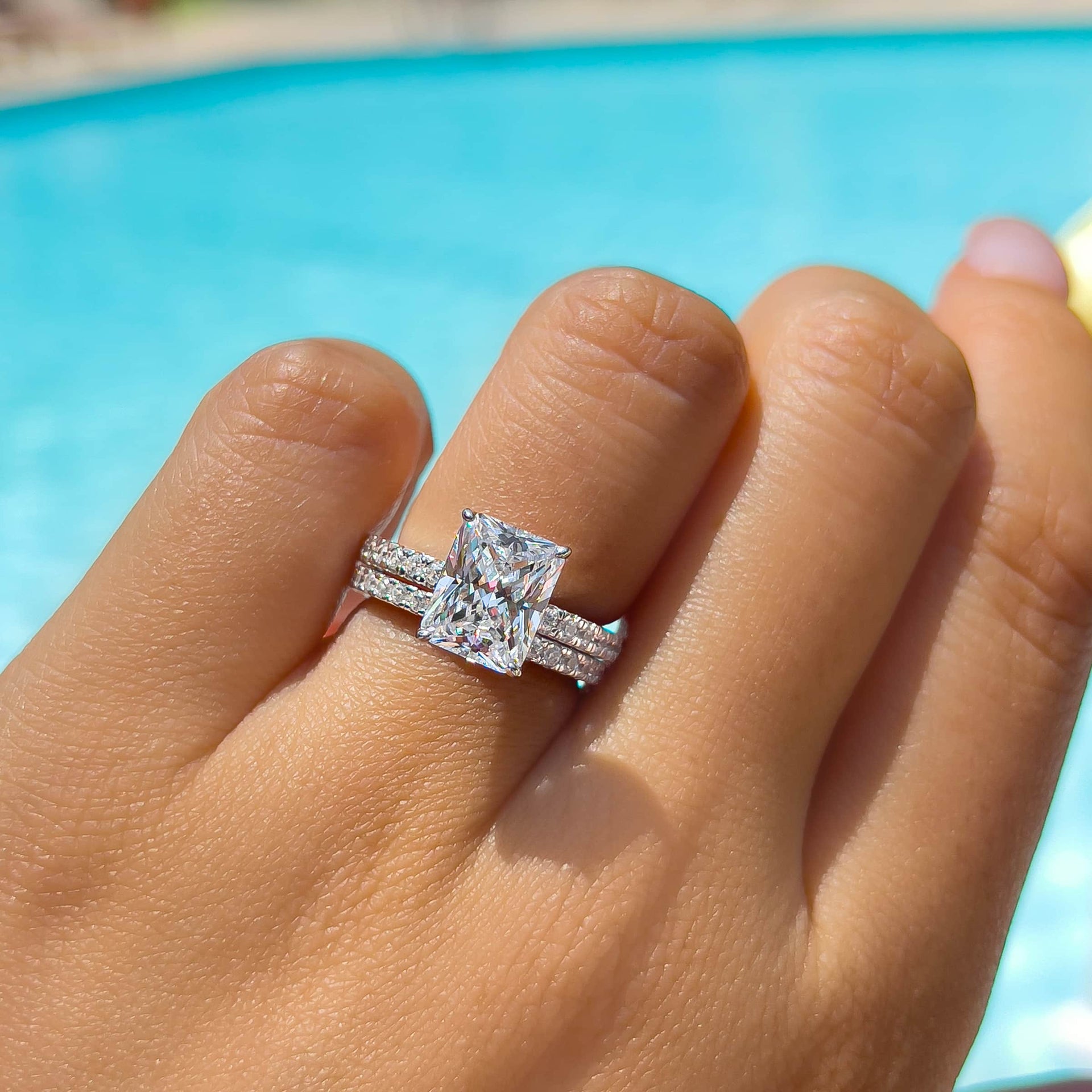 stunning radiant cut engagement ring paired with silver wedding band on model that is poolside