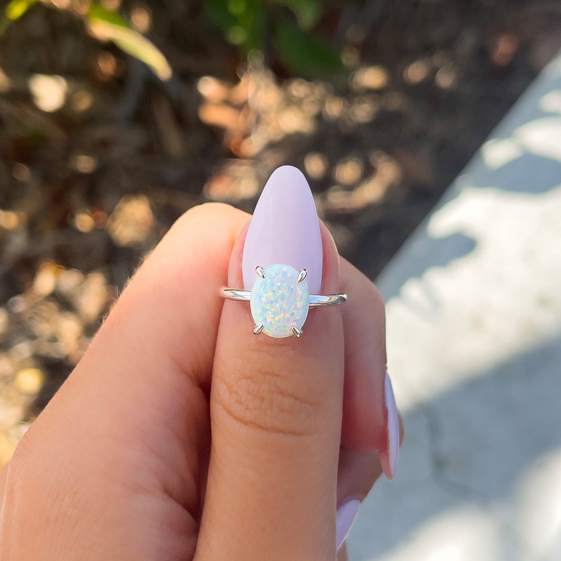 silver opal oval cut solitaire engagement ring held by model with light pink nails
