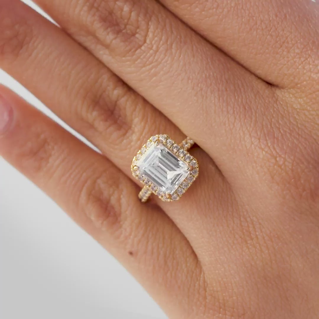 Multi-view video of stunning gold emerald cut engagement ring with a half eternity band, being shown by model with light pink nails