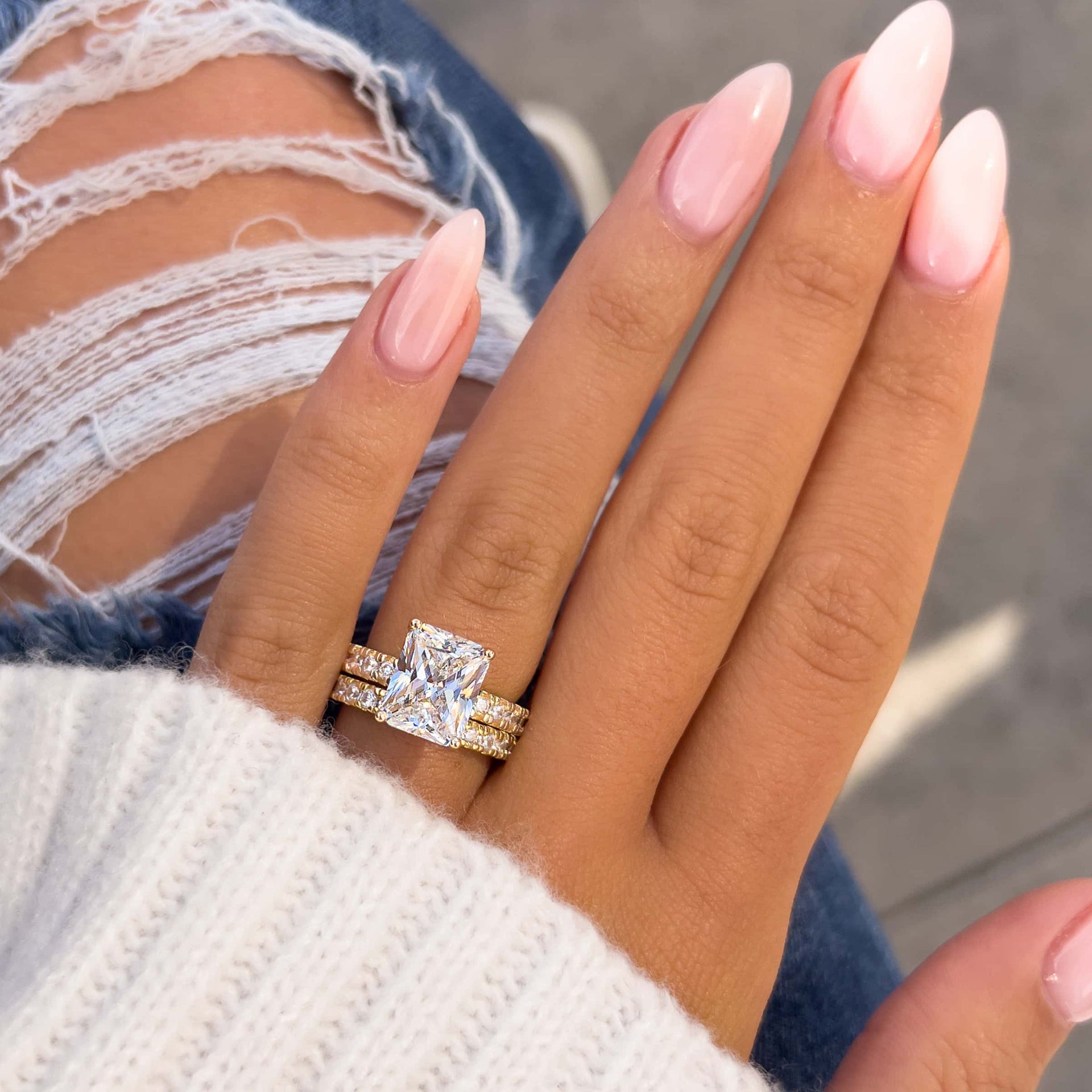 3.75 radiant cut engagement ring paired with gold eternity wedding band worn on model's hand with ripped jeans