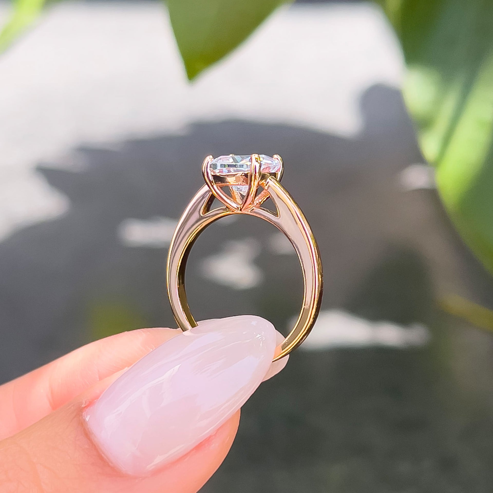 Setting shot of petite rose gold solitaire cushion cut engagement ring held by model with neutral colored nails
