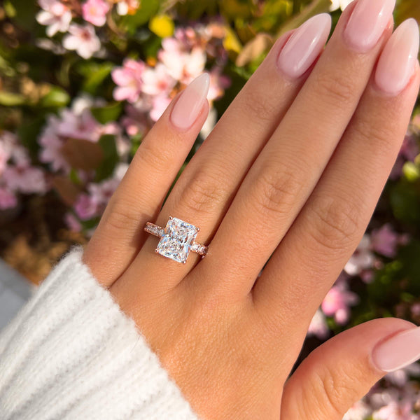 stunning rose gold radiant cut engagement ring with half eternity band modeled on female hand with flowers in background