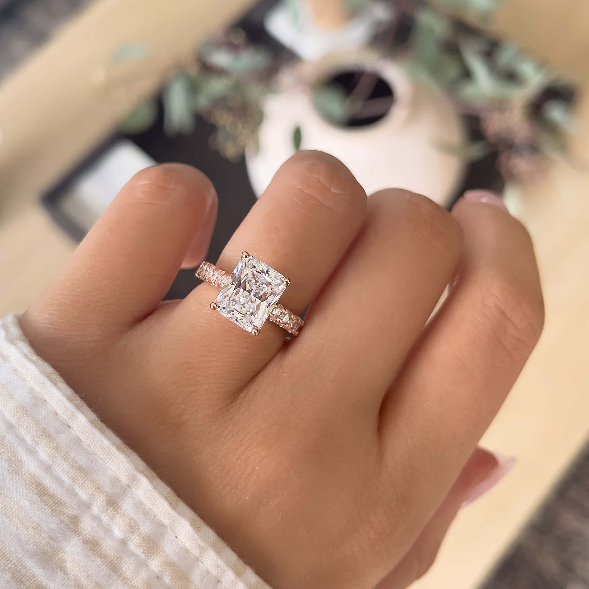 affordable radiant cut engagement ring in rose gold on female hand with white and brown sleeve