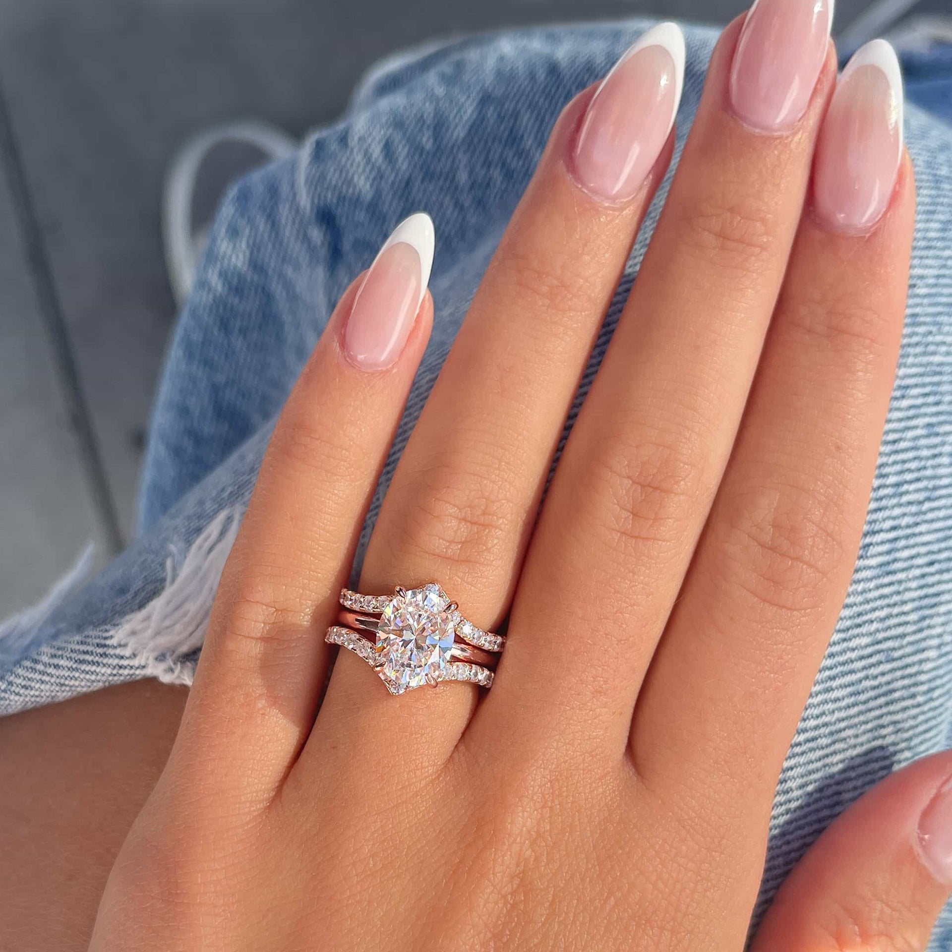 Two rose gold v-shaped half eternity wedding bands paired with a rose gold oval cut solitaire engagement ring modeled on female hand with French tip nails