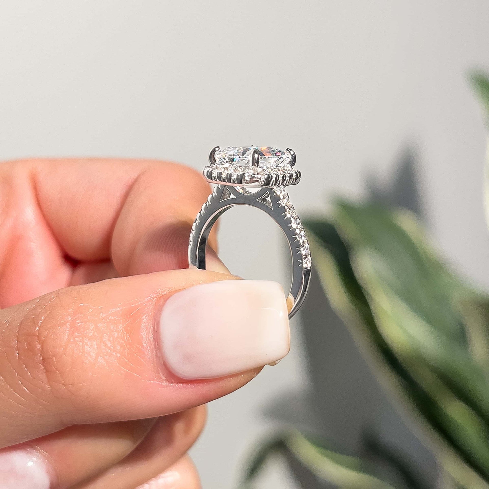 side profile of silver radiant cut engagement ring with half eternity band detailing being held by a model with milky white neutral nails