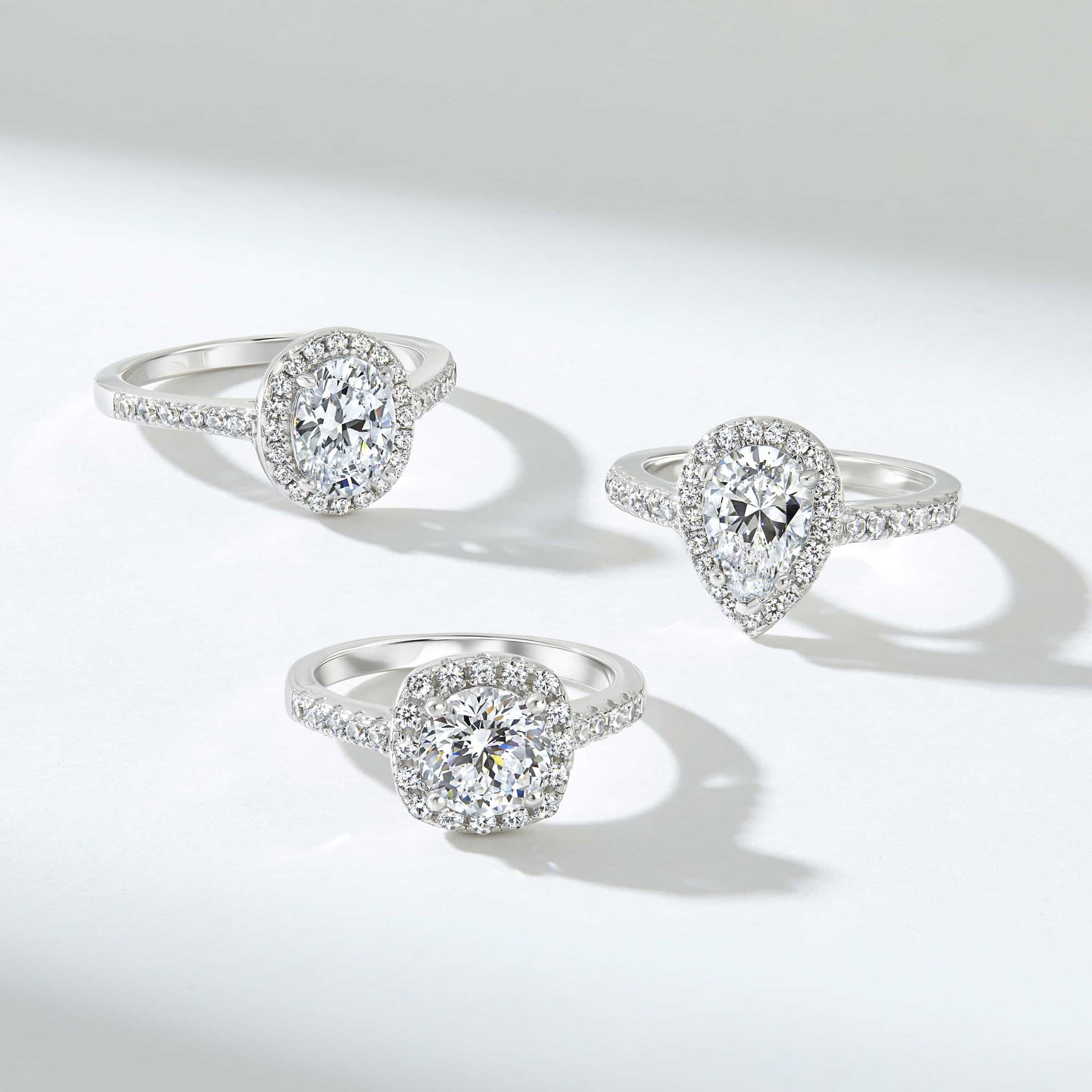 three silver engagement rings with halos placed on a grayish background