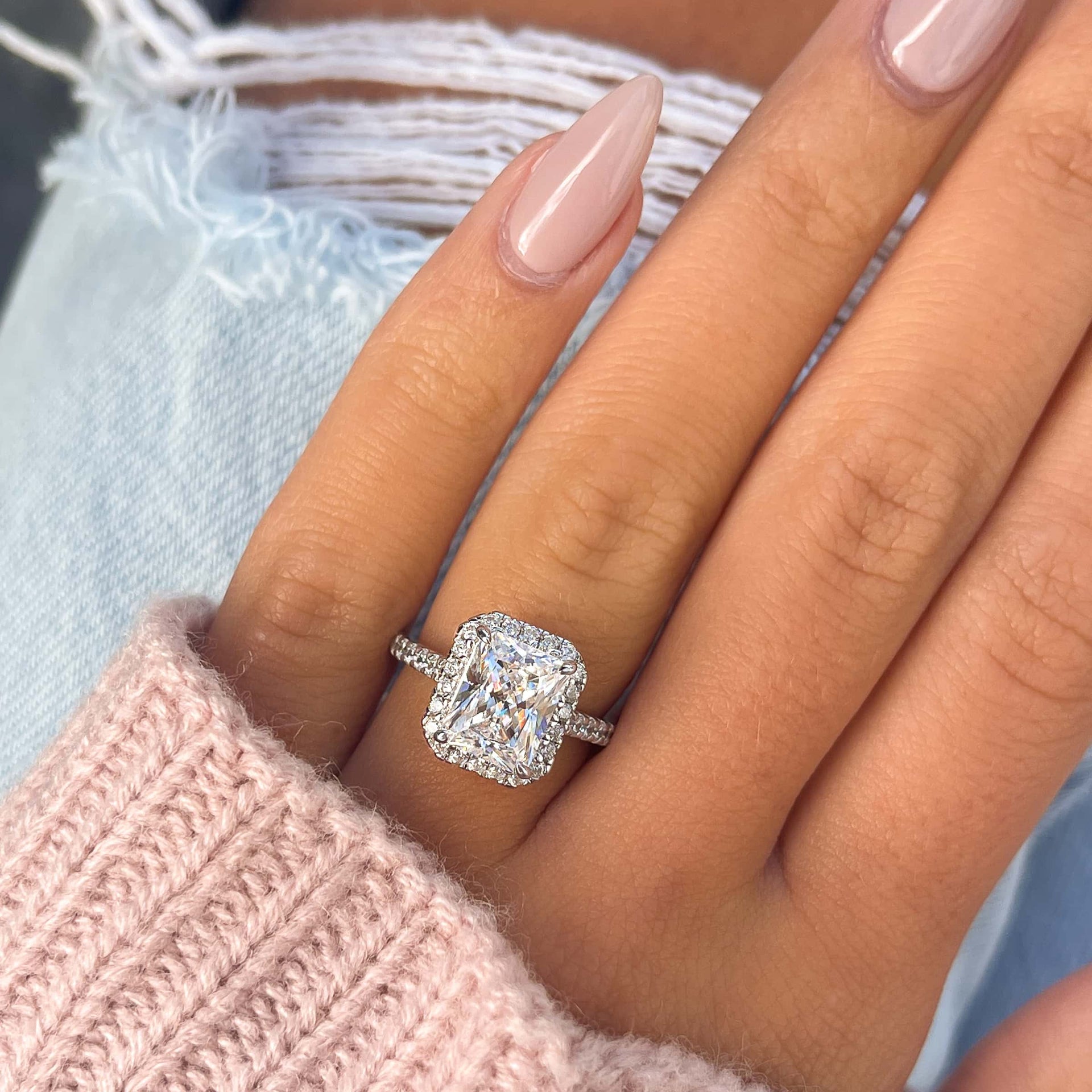 silver radiant cut engagement ring with halo and half eternity band detailing on female hand wearing a pink sweater