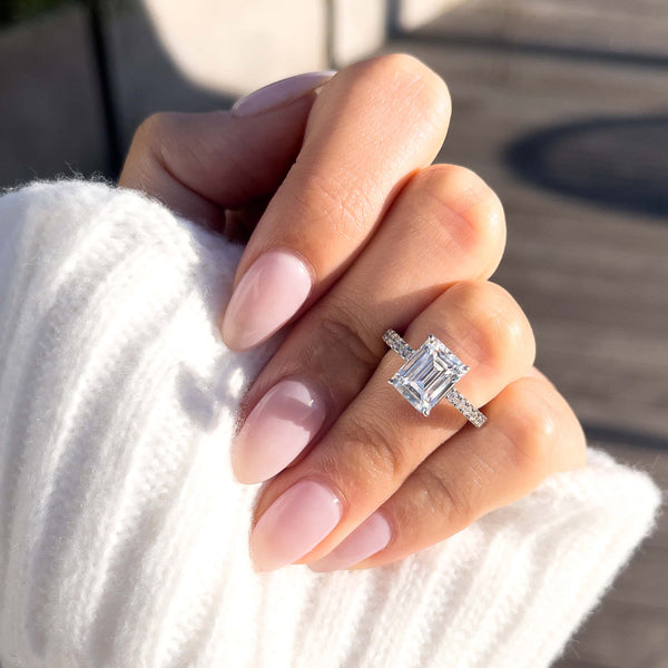modern 3 carat emerald cut silver engagement ring on female hand with white sweater