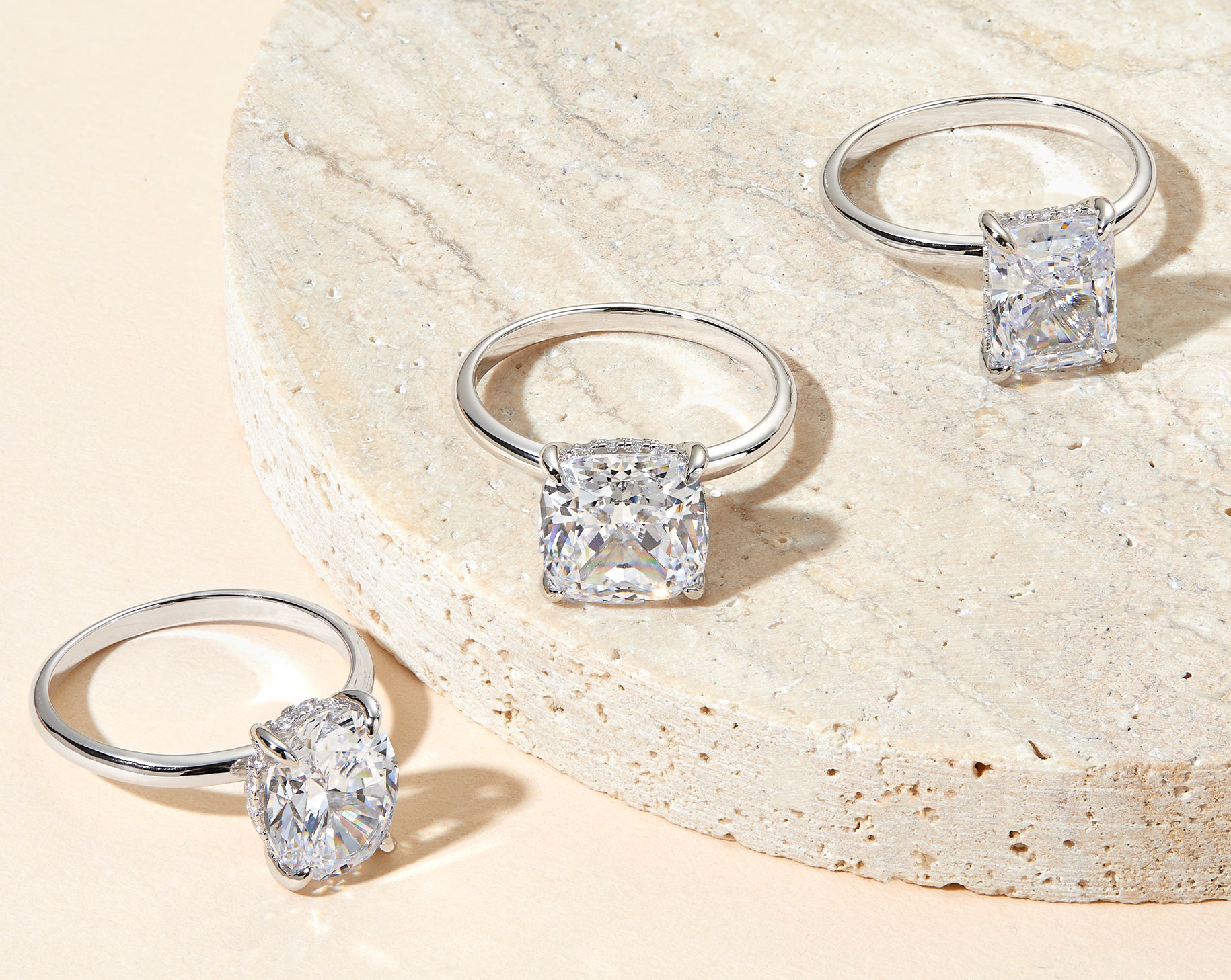 three solitaire silver engagement rings on neutral background
