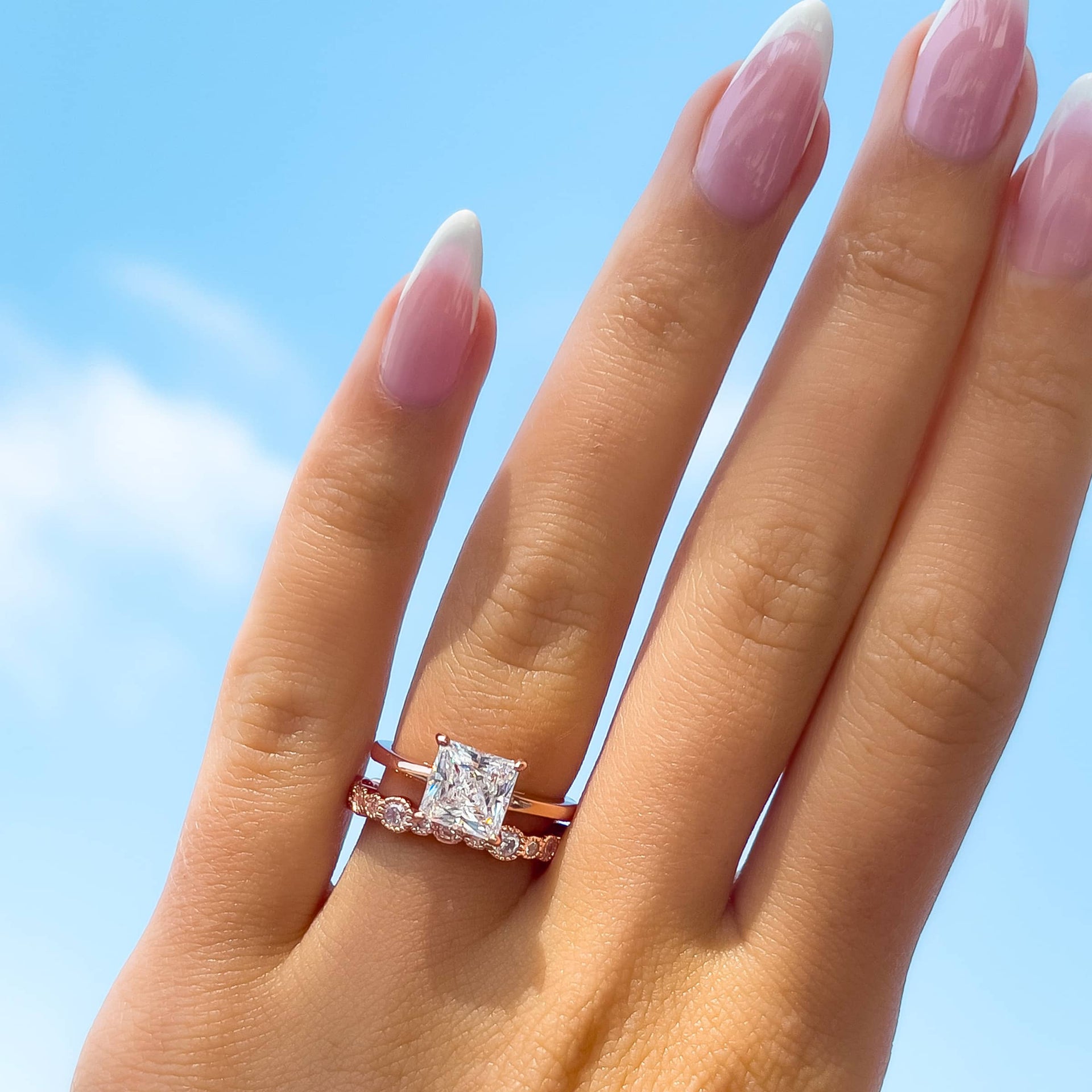 classic rose gold 2 carat princess cut solitaire engagement ring paired with unique rose gold wedding band on model with french tip nails