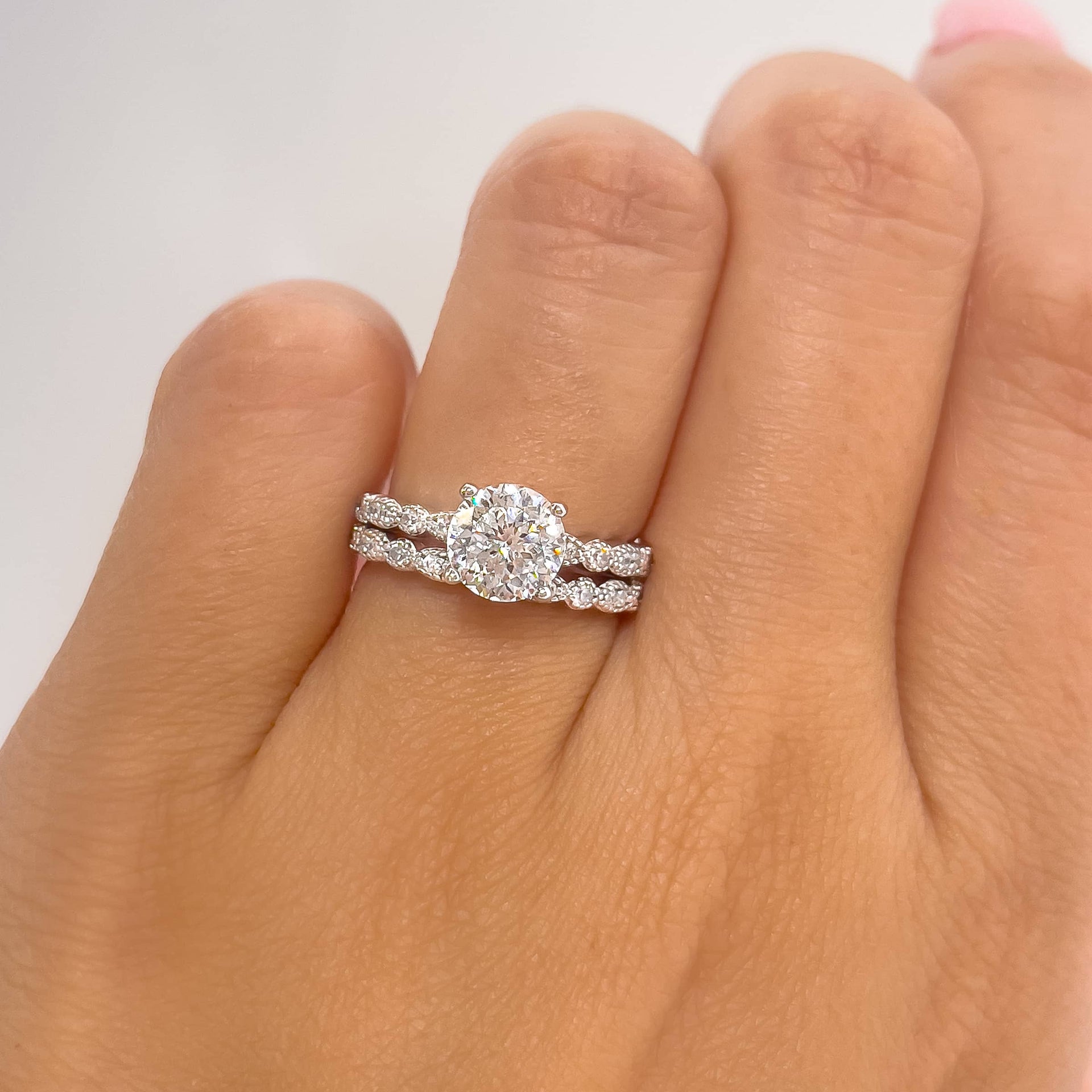 1.5 ct round cut silver engagement ring with complimentary silver vintage wedding band shown on woman's hand with white a background