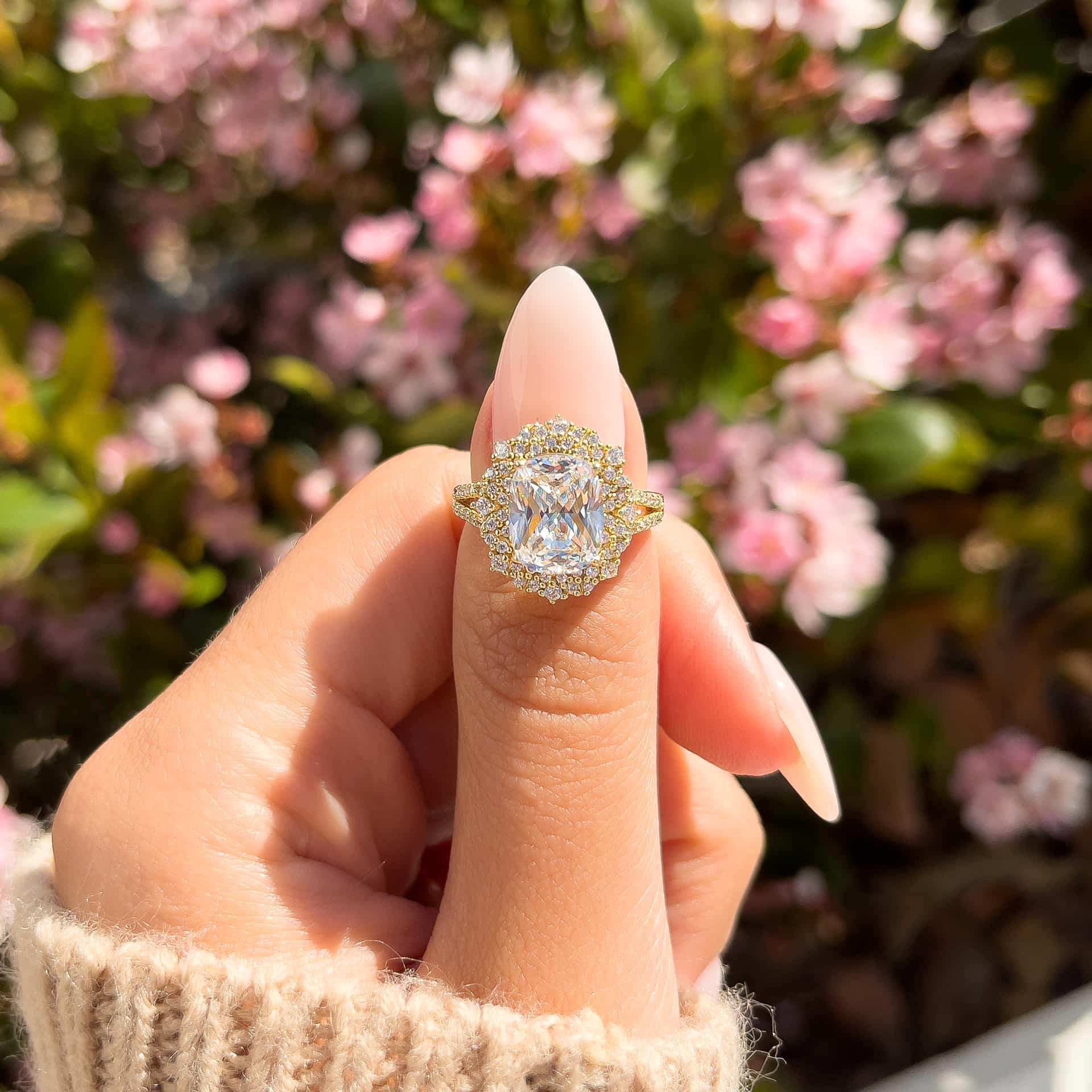 woman pinching gold sol engagement ring on finger with brown sweater and pink flowers in background