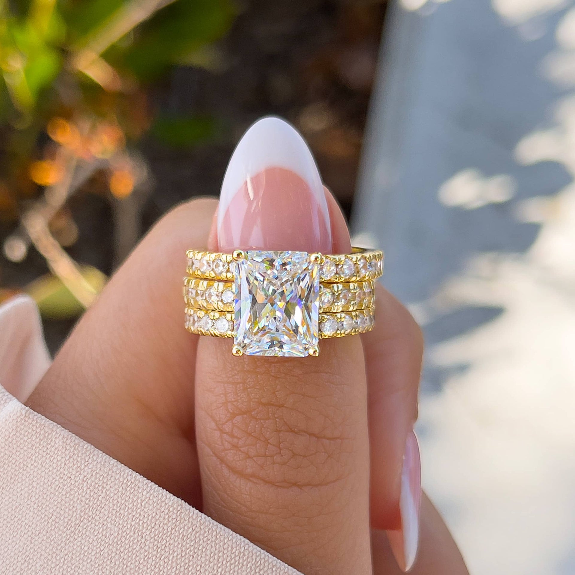 stunning gold radiant cut engagement ring with two matching gold wedding bands on model with french tip nails