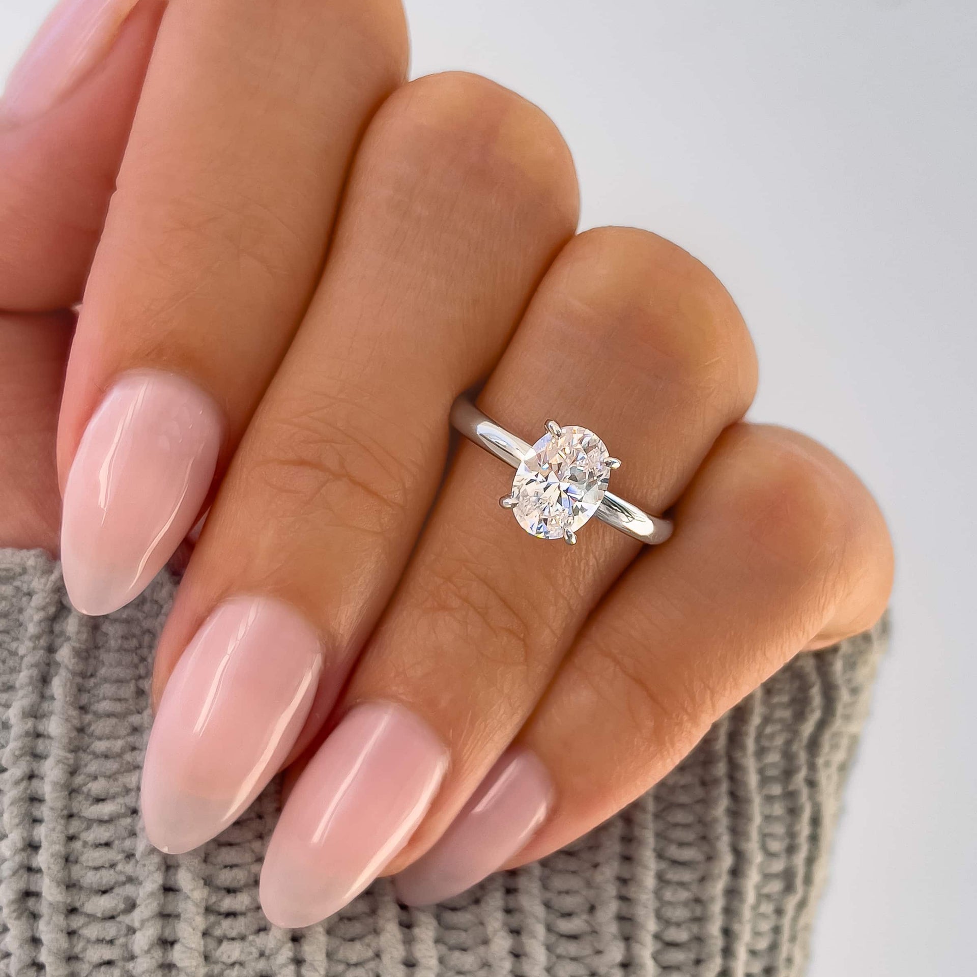 beautiful silver solitaire engagement ring on model with pink nails and gray sweater