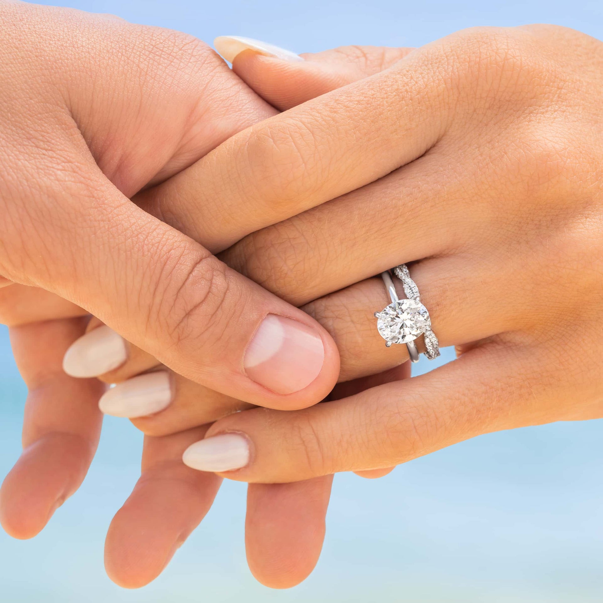couple holding hands wearing oval engagement ring