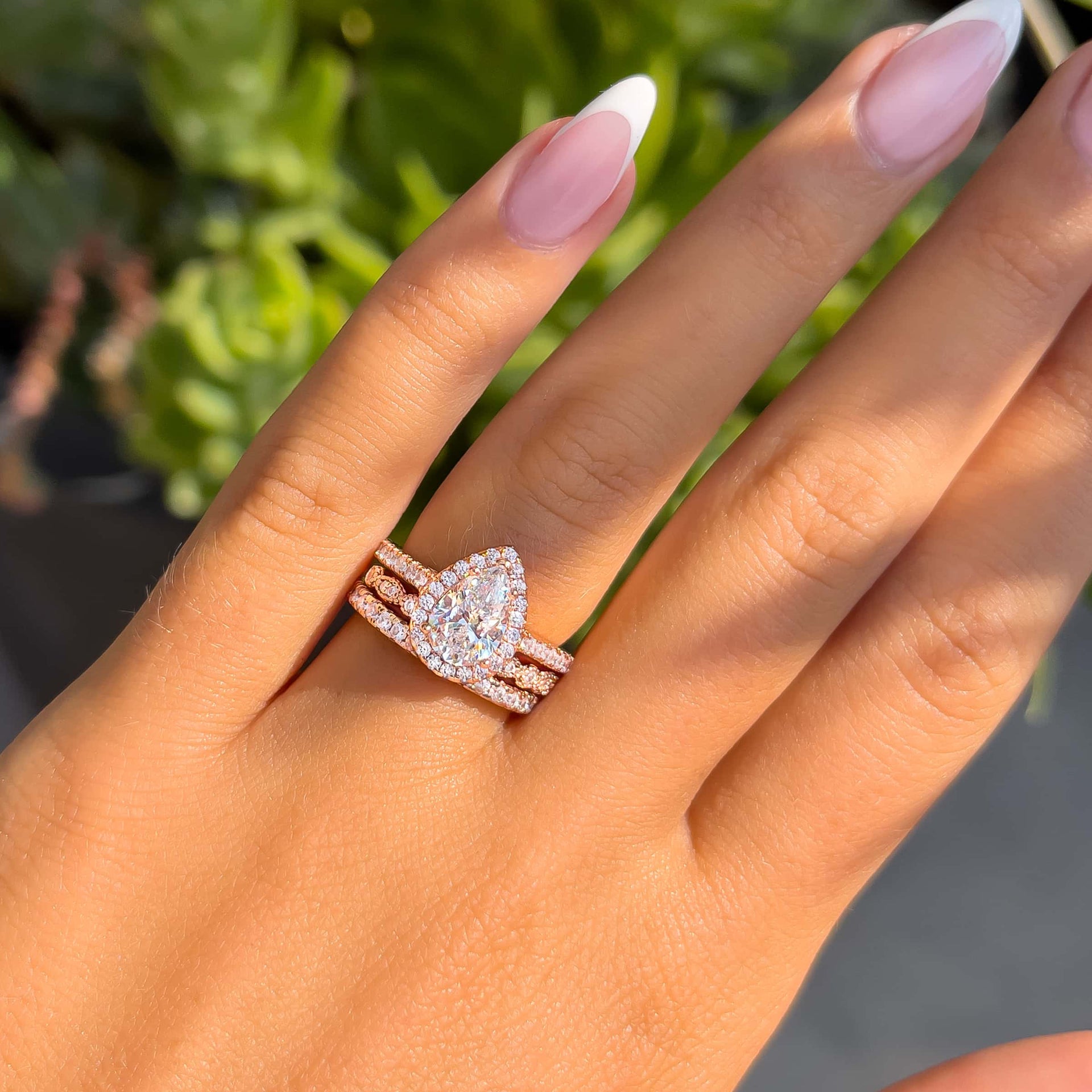 woman wearing pear shaped engagement ring with two complimentary wedding bands and greenery in background