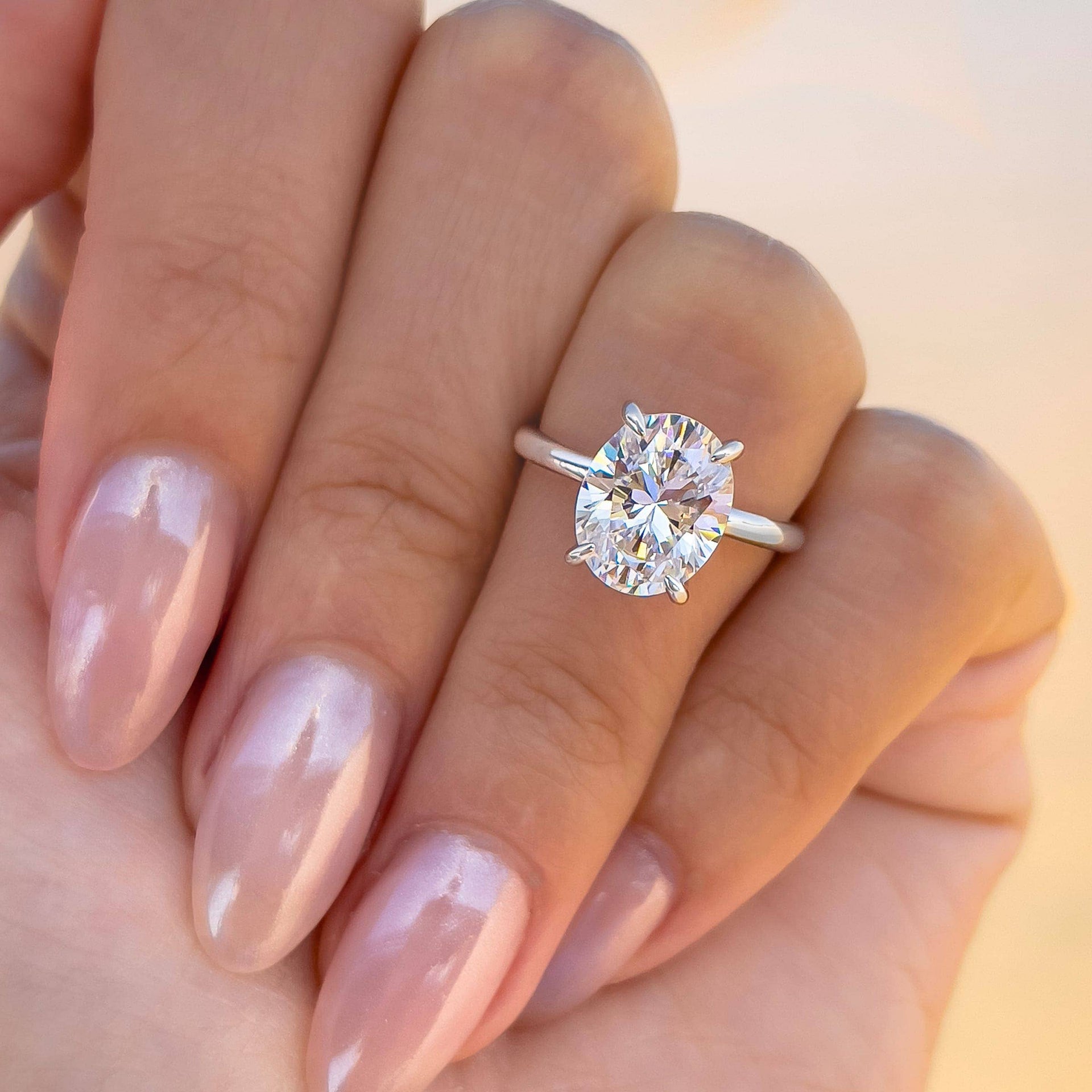 woman with oval silver solitaire engagement ring on hand with pink nails