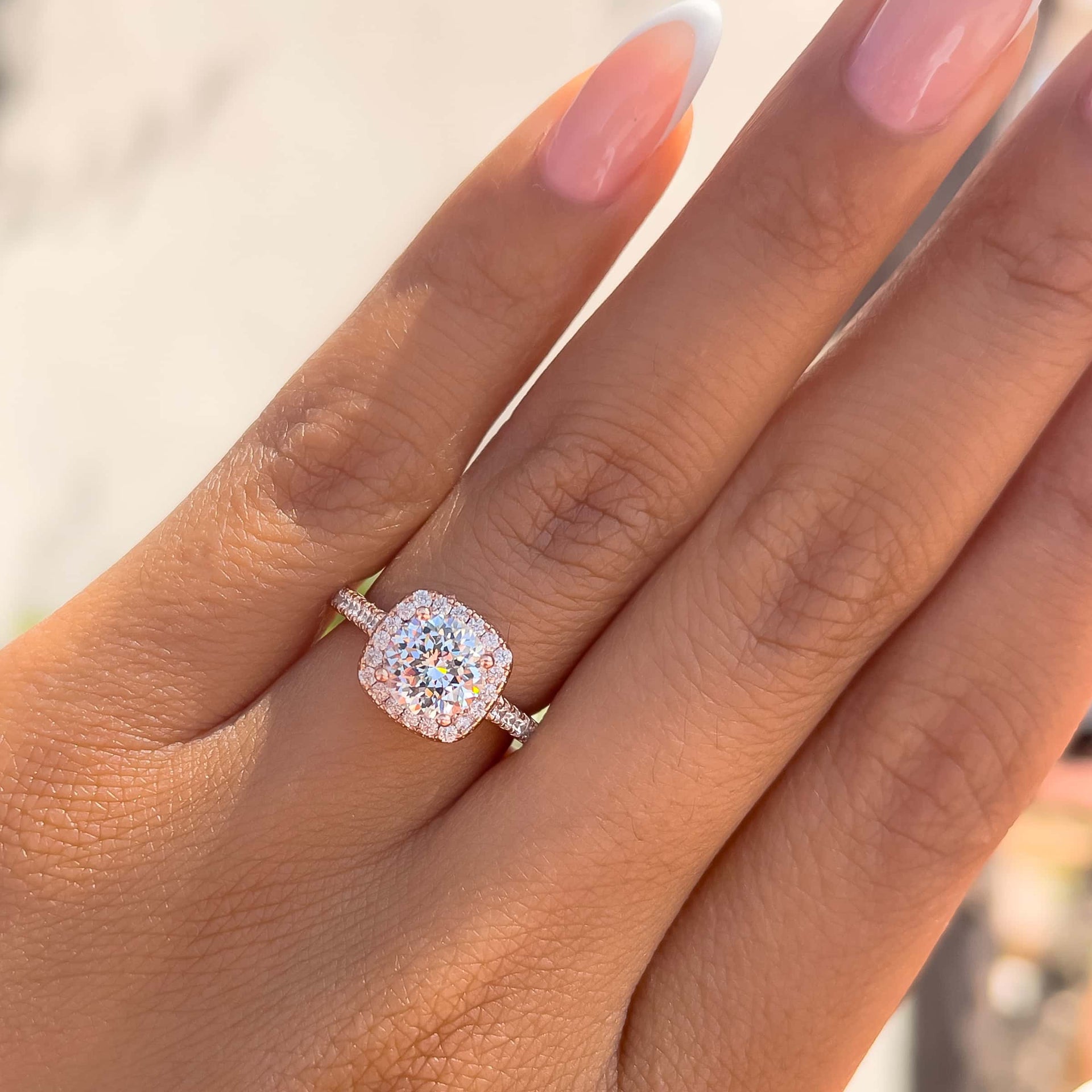 rose gold cushion cut engagement ring on ladies hand with neutral background and french tip nails