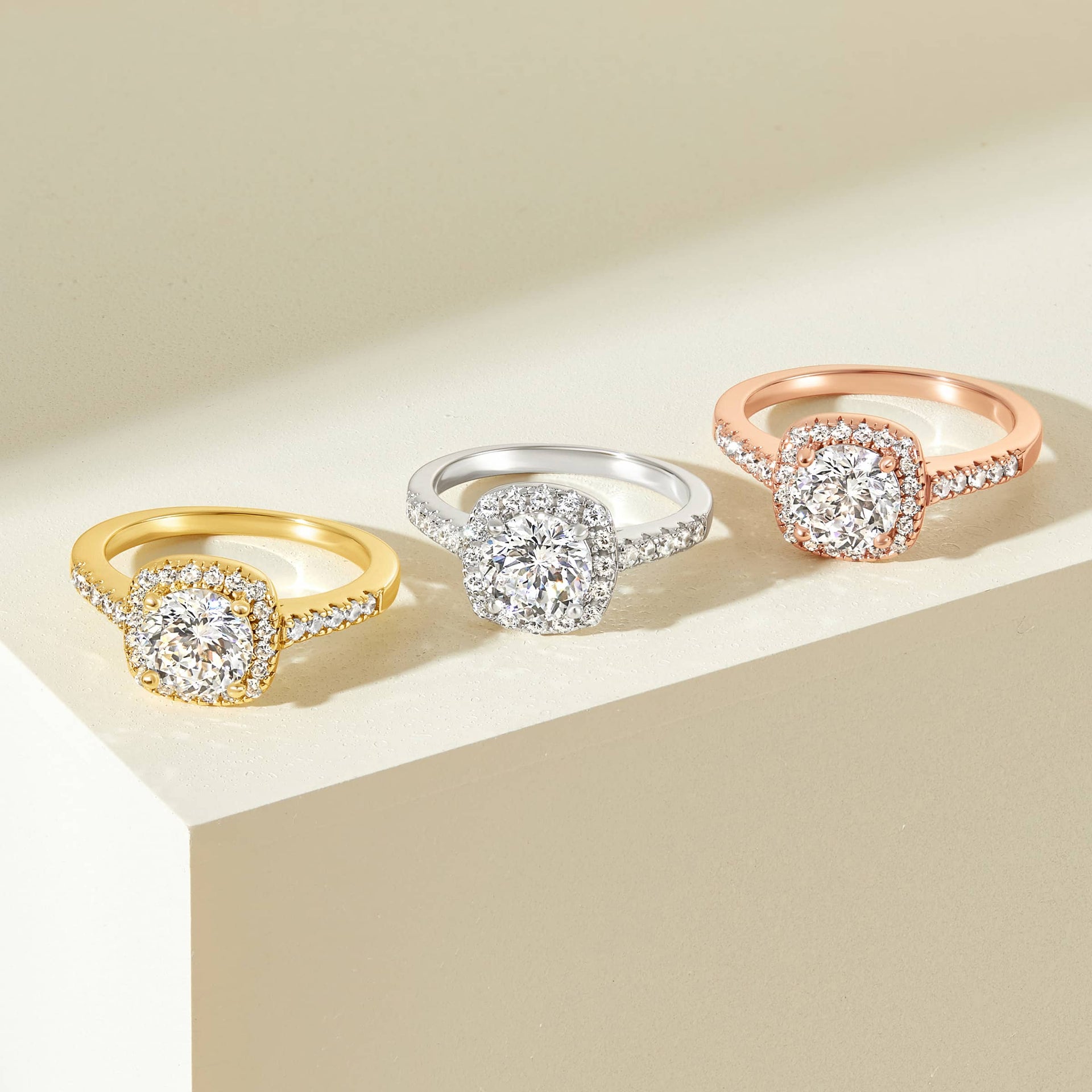 gorgeous flatlay showcasing gold, silver, rose gold cushion cut engagement rings on cream block