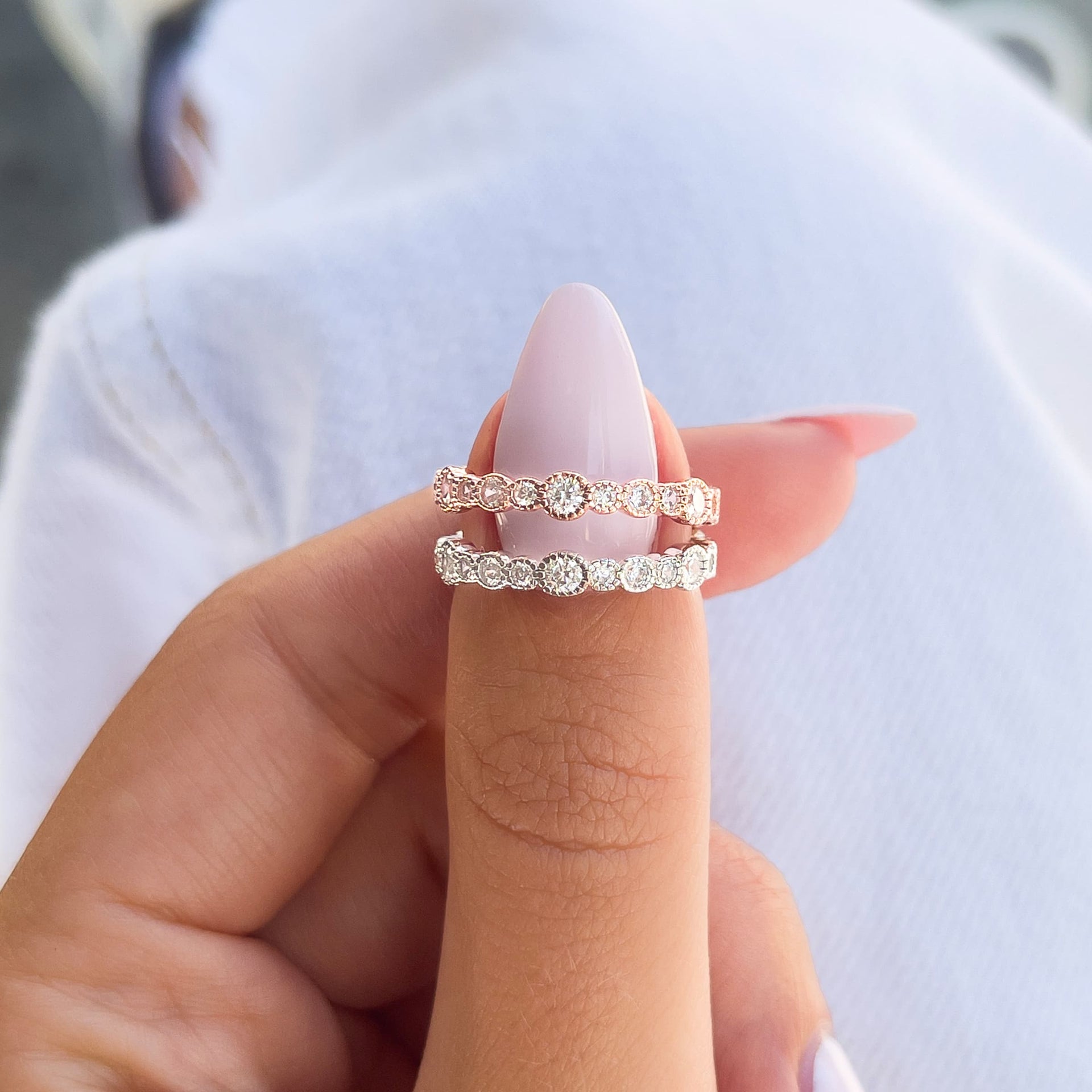 unique alternating stone size eternity wedding bands shown in silver and rose gold by model with light pink nails