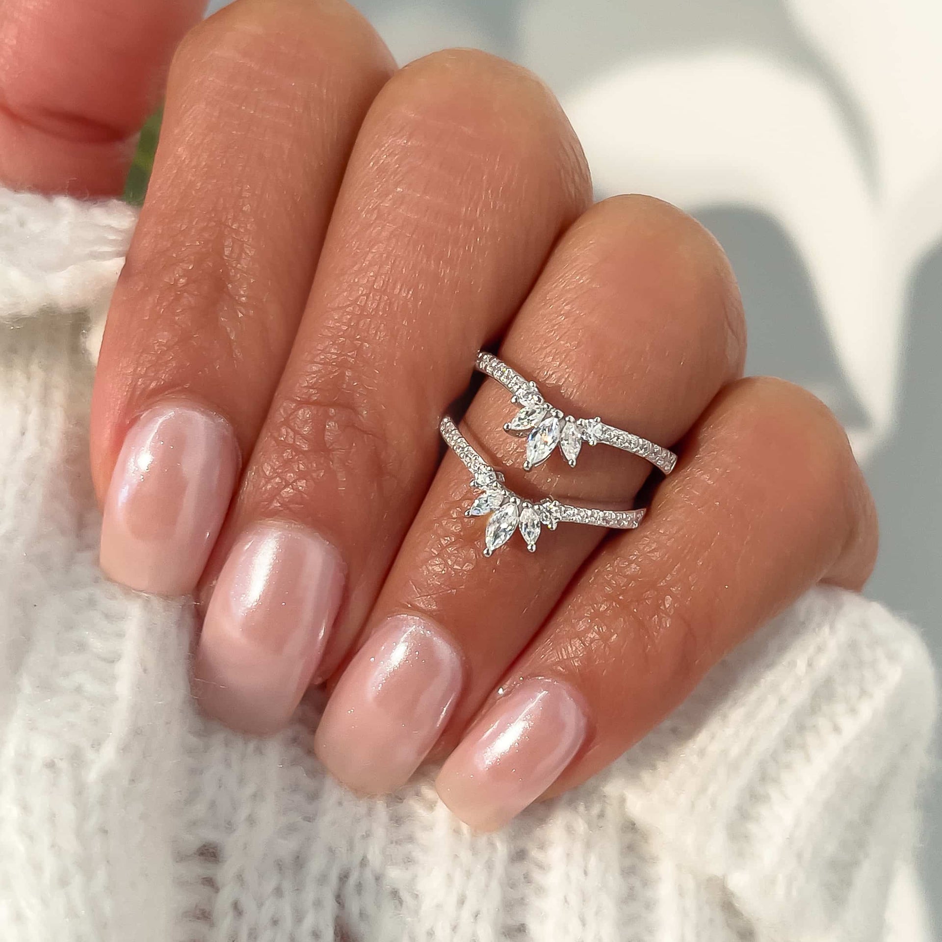 woman pinching two vintage engagement rings with white sweater and pink nails