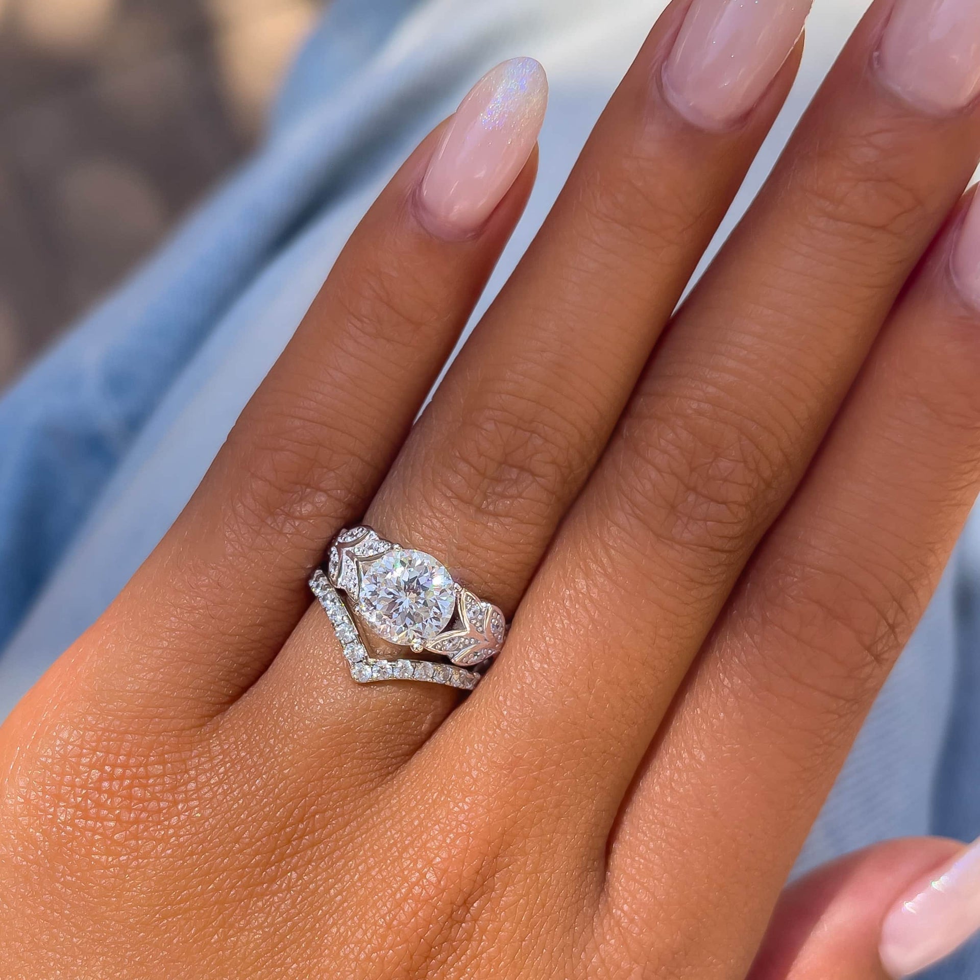 whimsical silver round cut engagement ring paired with v-shaped wedding band on model with neutral colored nails