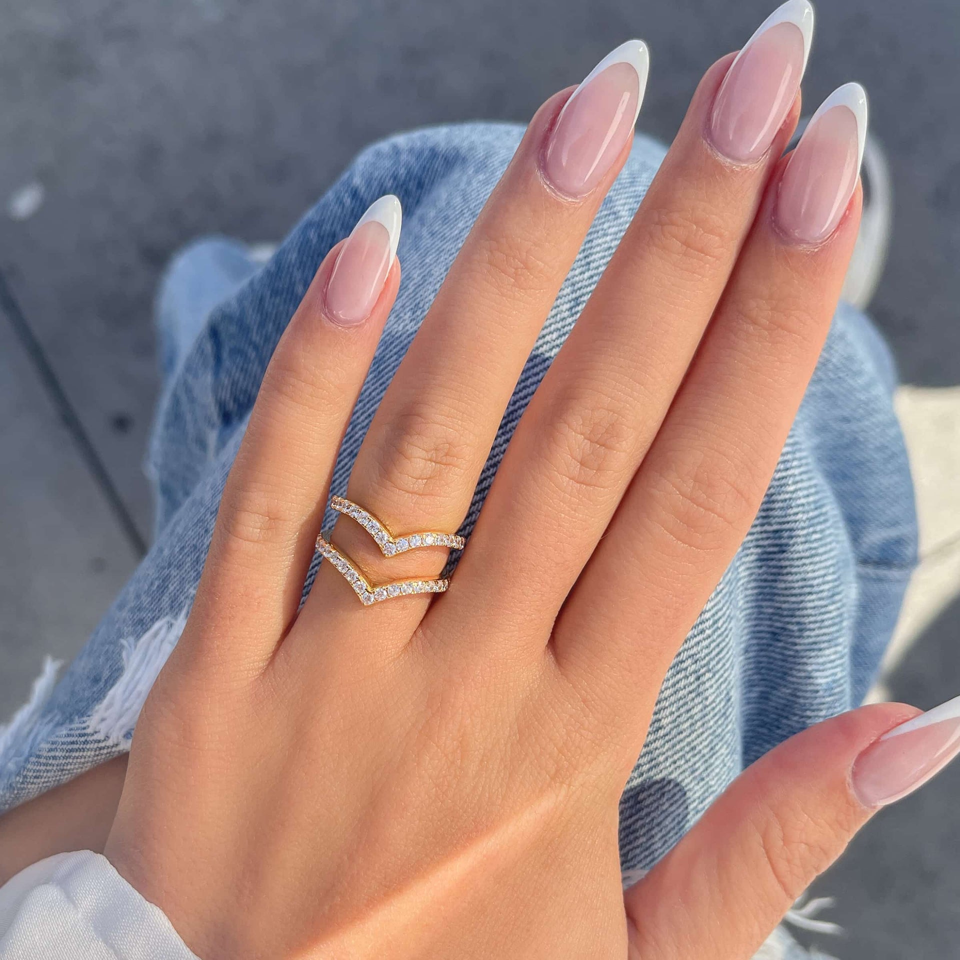 Half eternity chevron band set in the gold variant on hand with french tip nails resting on distressed jeans