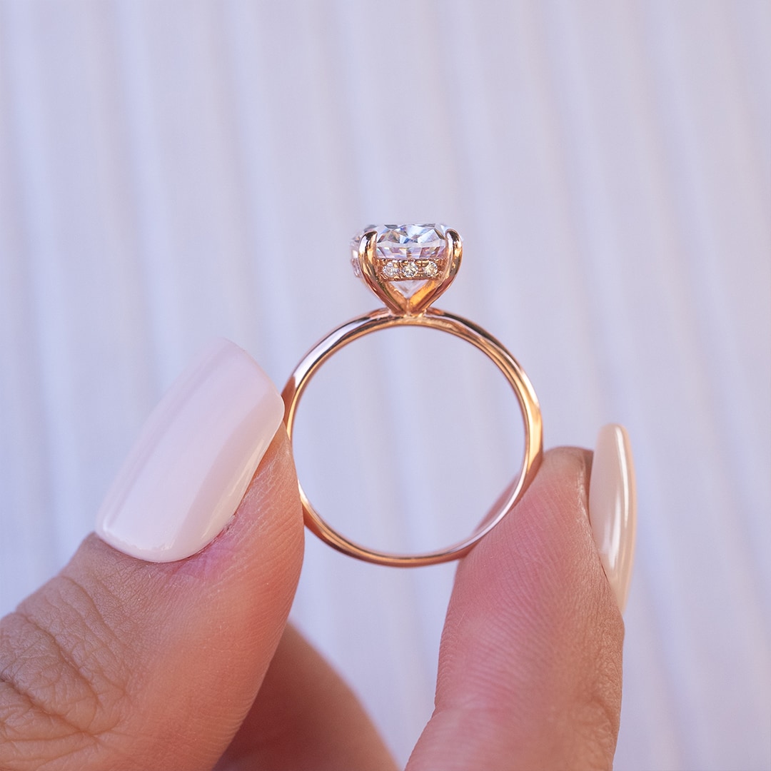 fingers holding rose gold oval solitaire engagement ring