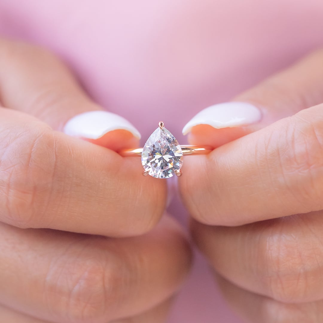 female hands holding rose gold pear engagement ring